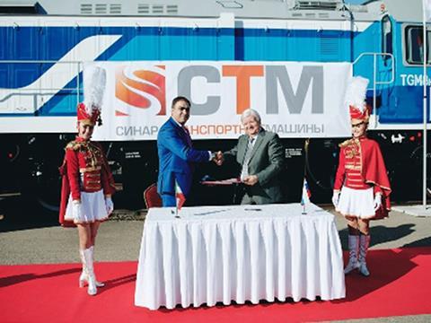 The contract was signed at the Expo 1520 trade show in Moscow. In the background is a TGM8KM diesel locomotive for Cuba, which was on display at the Sinara stand.